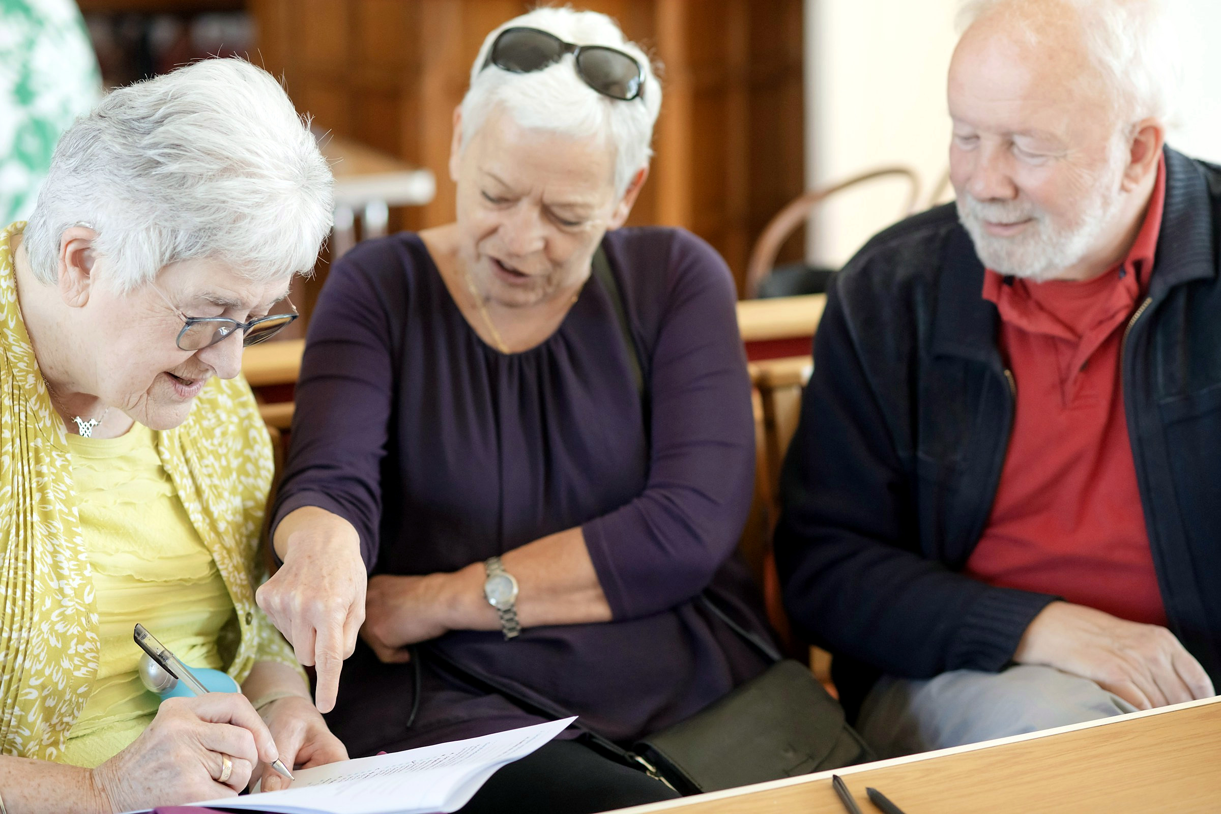 Three older adults reading through plan paperwork together at a table