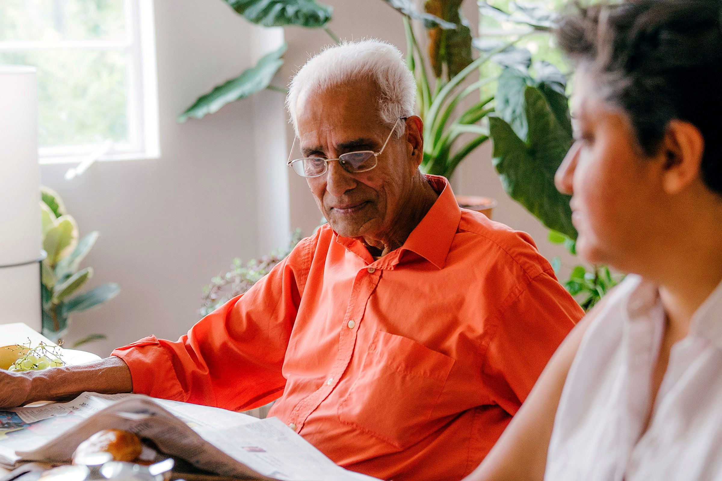 An older man talking something through with someone across a sunlit table